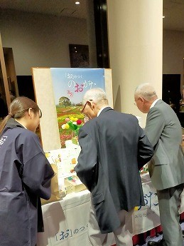 県人会会場で直方市の特産物を見る市長の写真