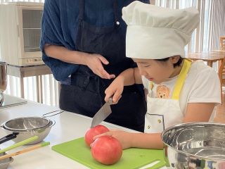 包丁でトマトの薄皮だけ切れ目を入れるお子さん